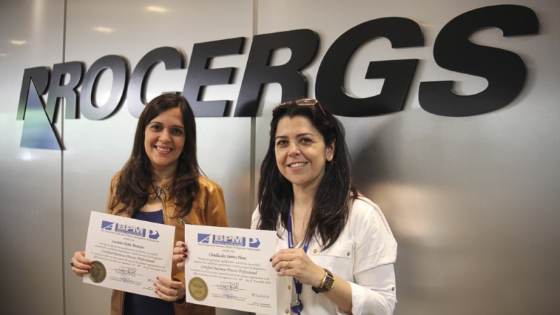 Funcionarias Luciana Hahn Menezes e Cláudia dos Santos Flores segurando certificados em frente à marca da Procergs