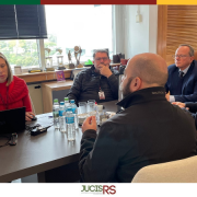 Sala de reuni&otilde;es com 5 pessoas sentadas em volta de uma mesa retangular e marrom. 
