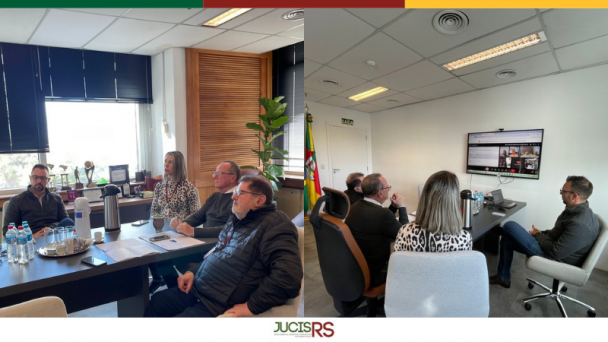 Sala de reuni&otilde;es com 4 pessoas sentadas em tono de uma mesa retangular e marrom. 